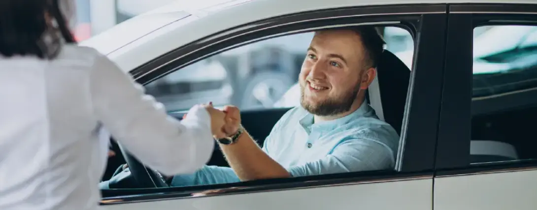 Homem feliz dentro de carro recebendo a chave de vendedora