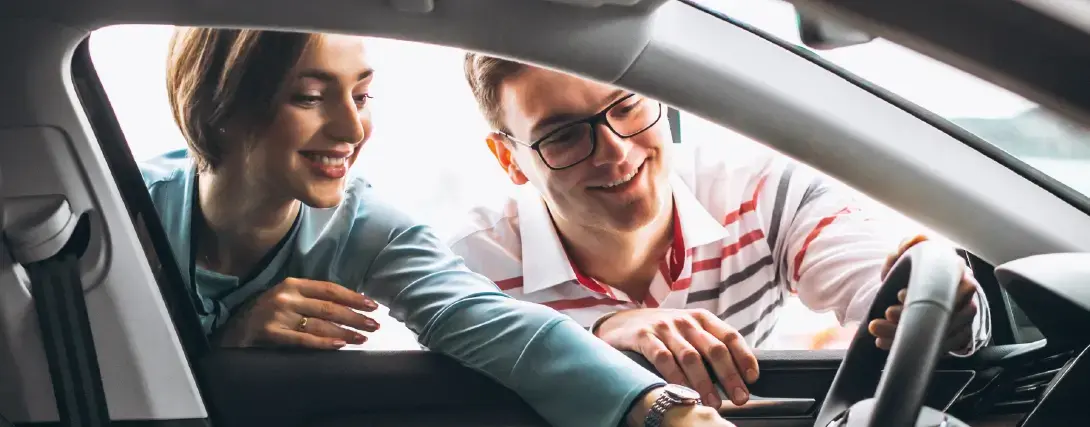 Vendedora sorridente apresentando o carro para um cliente feliz