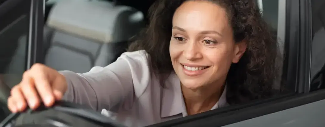 Mulher motorista de aplicativo segurando o volante e sorrindo dentro do carro